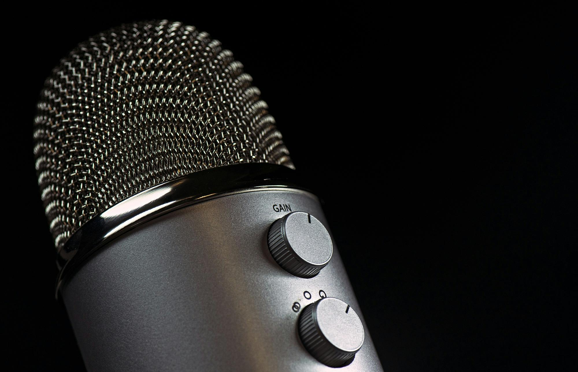 Detailed close-up of a silver mesh microphone with gain control knobs against a dark background.